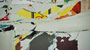 Close-up of a layered collage made from torn strips of colourful printed paper, showing rough edges and overlapping textures